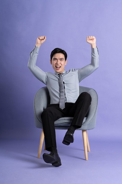 Portrait of Asian business man sitting on sofa isolated on purple background