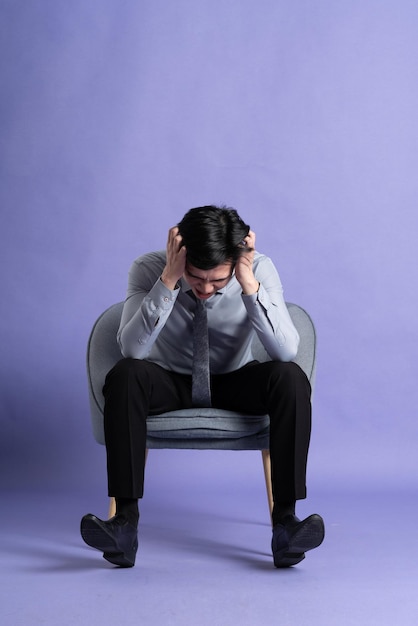 Portrait of Asian business man sitting on sofa isolated on purple background