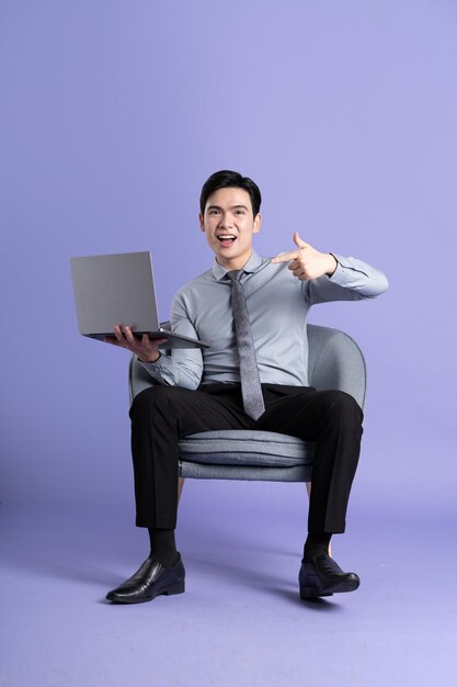 Portrait of Asian business man sitting on sofa isolated on purple background