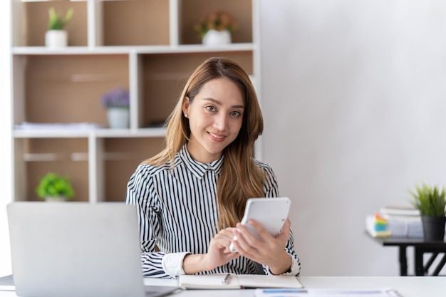 Photo portrait of asian business woman paying bills online with laptop in office beautiful girl with computer and chequebook happy paying bills startup business financial calculate account concept