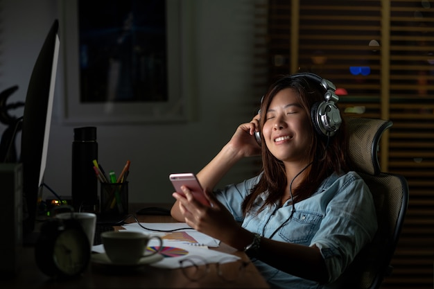 Portrait of Asian Businesswoman listening the music via headphone and smart mobile phone