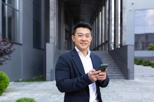 Portrait of Asian cheerful and successful businessman near office in business suit got good news read good news online