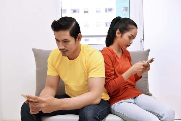 Portrait of asian couple busy with their mobile phones in their hand