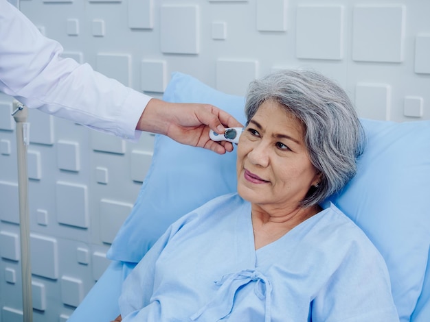 Portrait of Asian elderly woman patient on bed is being measured checked by temperature in the ear with tympanic thermometer by doctor in hospital or clinic Healthcare and medical checking concept