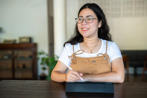 Portrait asian freelance people business female wearing glasses stylish hipste Draw or taking note on digital tablet with electronic pen for browsing internet chatting and blogging in coffee shop