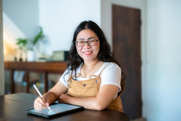 Portrait asian freelance people business female wearing glasses stylish hipste Draw or taking note on digital tablet with electronic pen for browsing internet chatting and blogging in coffee shop