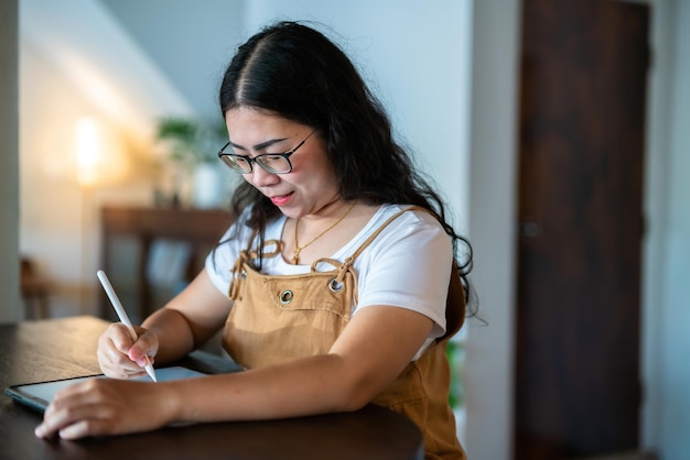 Portrait asian freelance people business female wearing glasses stylish hipste Draw or taking note on digital tablet with electronic pen for browsing internet chatting and blogging in coffee shop