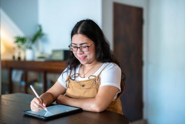 Portrait asian freelance people business female wearing glasses stylish hipste Draw or taking note on digital tablet with electronic pen for browsing internet chatting and blogging in coffee shop