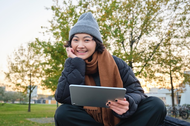 Portrait of asian girl relaxing in park watching videos or reading on digital tablet sitting on benc