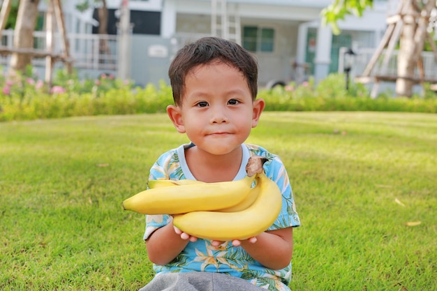 Portrait of Asian little boy age about 5 years old holding yellow banana in the garden