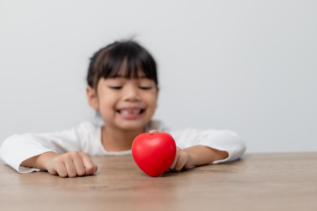 Portrait of Asian little girl child holding red heart sign on white background