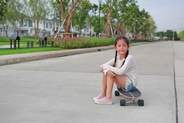 Portrait of Asian little girl child sitting on a skateboard on the road