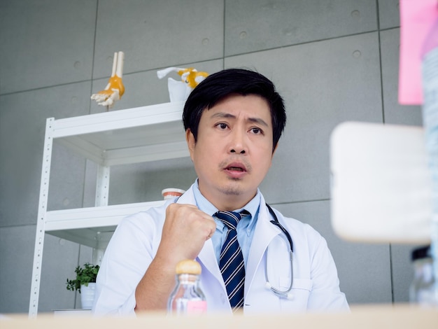 Portrait of Asian male doctor in white uniform with a stethoscope looking at camera on smart mobile phone screen online video call and encourage patient Healthcare medical and Telemedicine concept