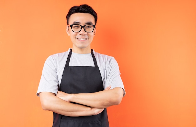 Portrait of Asian male waiter posing on orange wall