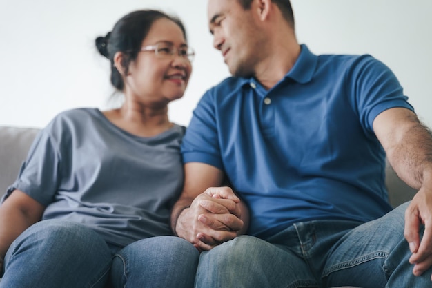 Portrait of Asian mature couple sitting in the living room wife and husband hugging holding hand