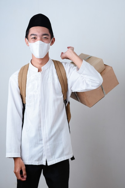 Portrait Asian Muslim man against on grey wearing muslim clothes and holding the box of gifts with a backpack