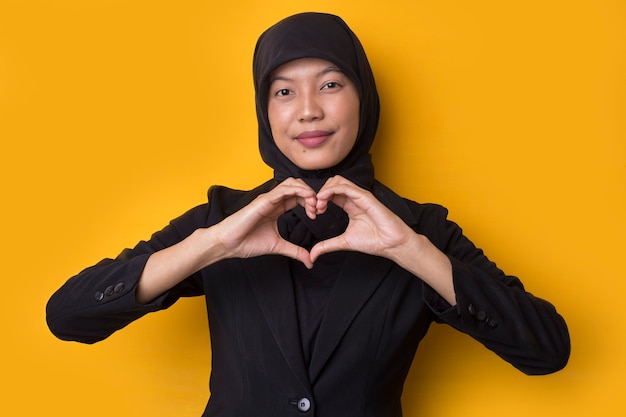 Portrait asian muslim woman showing heart sign on yellow space