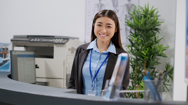 Portrait of asian receptionist working with checkup papers at hospital registration counter, using report forms. Medical worker analyzing insurance support files at reception desk in facility lobby.