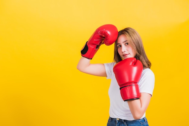 Portrait Asian Thai beautiful young woman standing smile wearing red boxing gloves she poses like a boxer, studio shot isolated on yellow background, There was copy space for text