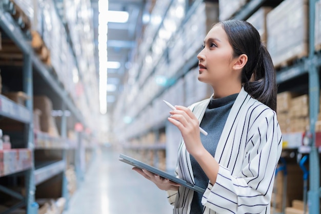 Portrait of asian woman business owner using digital tablet checking amount of stock product inventory on shelf at distribution warehouse factorylogistic business shipping and delivery service