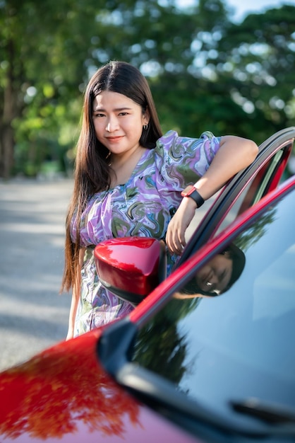 Portrait asian woman Wear purple dress wearing smartwatch in the car door modern red car at the city park outdoors