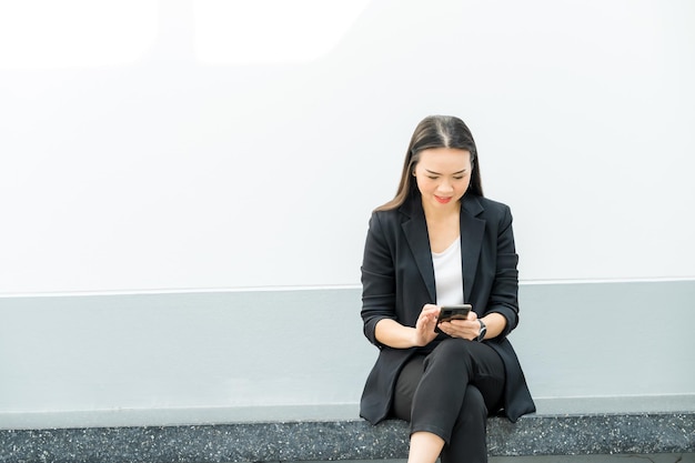 Photo portrait of an asian working woman wearing a black suit holding a mobile phone connected to the internet to send job information. concept of using internet technology in daily life