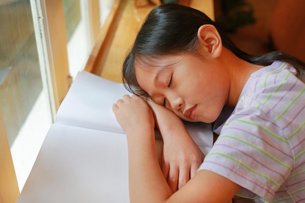 Portrait of Asian young girl child sleeping on a book near the windows Education and resting concept