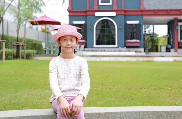 Portrait of Asian young girl child wearing pink straw hat sitting in the garden