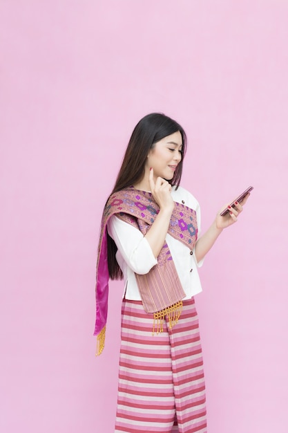 Portrait of asian young girl in traditional thai dress and holding smartphone on pink back