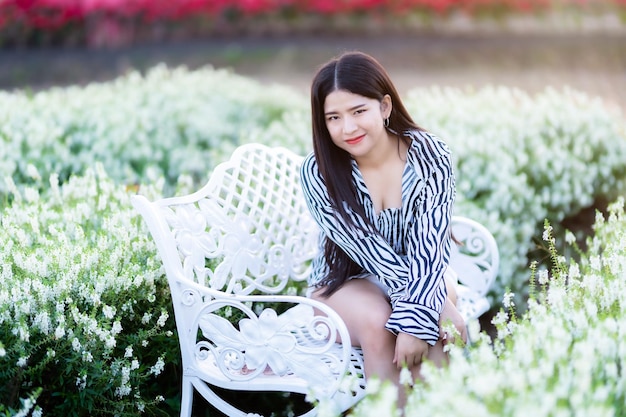 Portrait of asian Young woman happy traveler with black and white pattern dress enjoying sitting on white bench in white blooming flower field in the nature garden of in Thailandtravel relax vacation