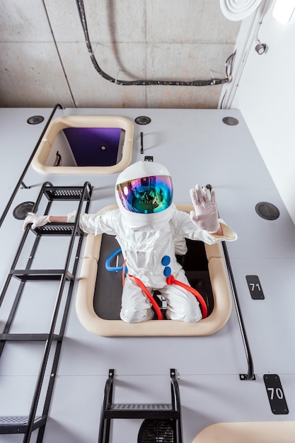 Portrait of an astronaut in a space suit saying hello to the sleeping module of the capsule hotel