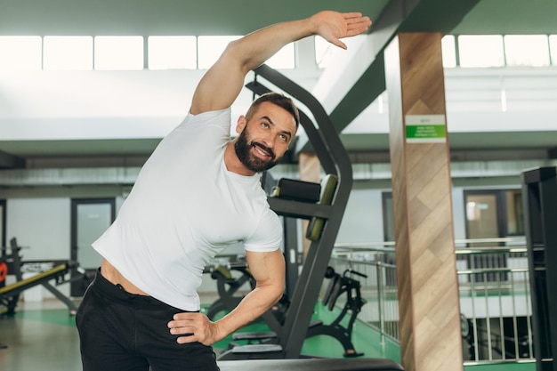 Portrait of an athlete in the gym A man wearing a white Tshirt is smiling and doing exercises