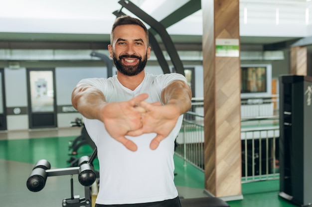 Portrait of an athlete in the gym A man wearing a white Tshirt is smiling and doing exercises