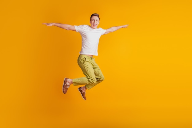 Photo portrait of athletic energetic active guy jump pretend airplane hands wings on yellow background