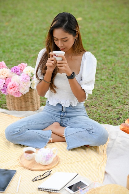 Portrait Attractive Asian young woman tasting an afternoon tea during picnic in the greenery park