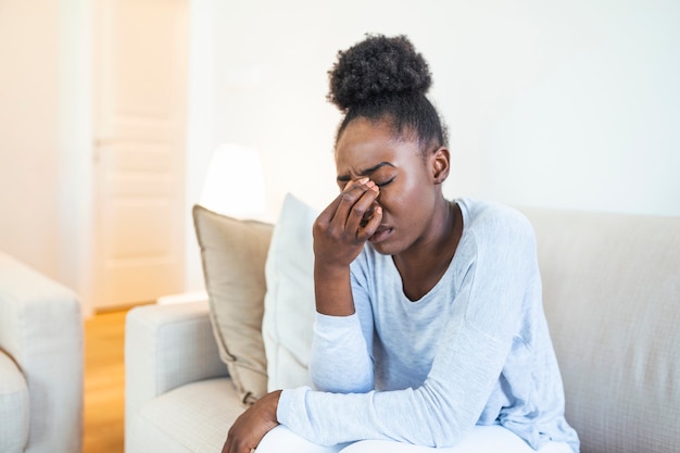 Portrait of an attractive black woman sitting on a sofa at home with a headache