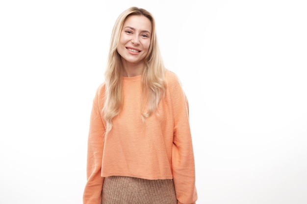 Portrait of attractive blonde girl in orange casual posing and smiling joyfully isolated on white studio background