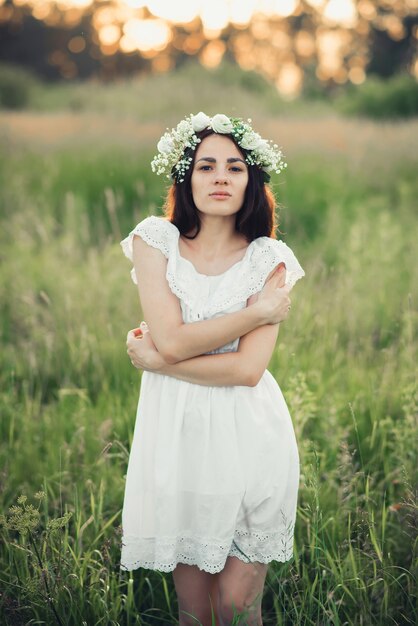 Portrait of attractive brunette girl in white dress and with floral wreath