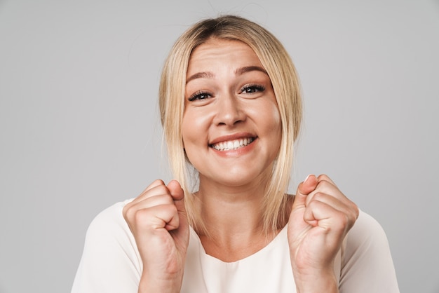 Portrait of an attractive casual woman standing isolated over gray wall, celebrating success