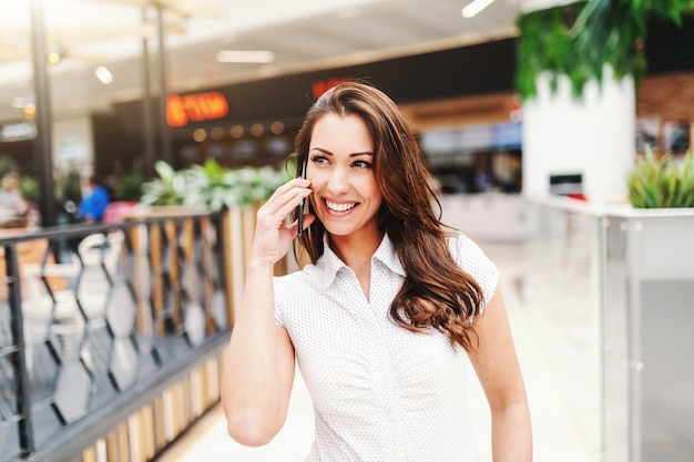 Portrait of attractive caucasian woman with long brown hair dressed casual using smart phone in shopping mall.