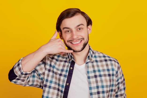 Photo portrait of attractive cheerful guy happy positive smile showing call me sign answer isolated over yellow color background