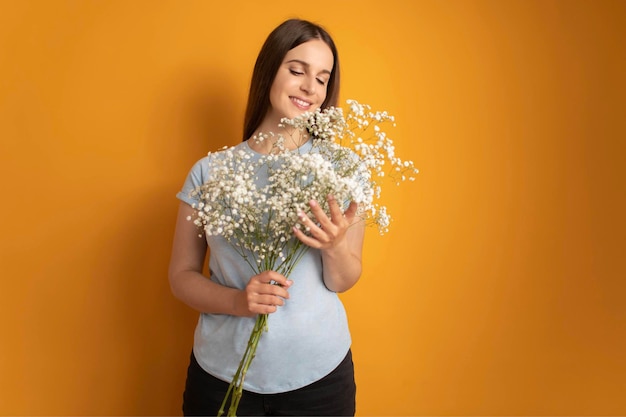 Portrait of attractive cheerful minded dreamy girl holding flowers gypsophila yellow color backgroun