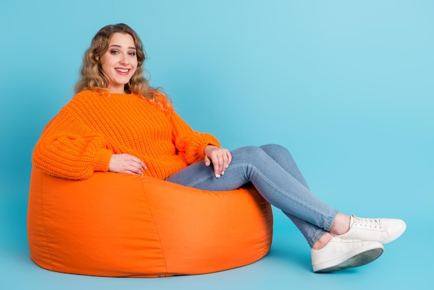 Photo portrait of attractive dreamy cheerful girl sitting in bag chair resting free time isolated over green teal color background