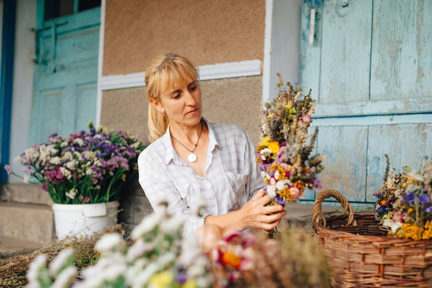 Portrait of an attractive female florist creates a bouquet of dried flowers with a serious face