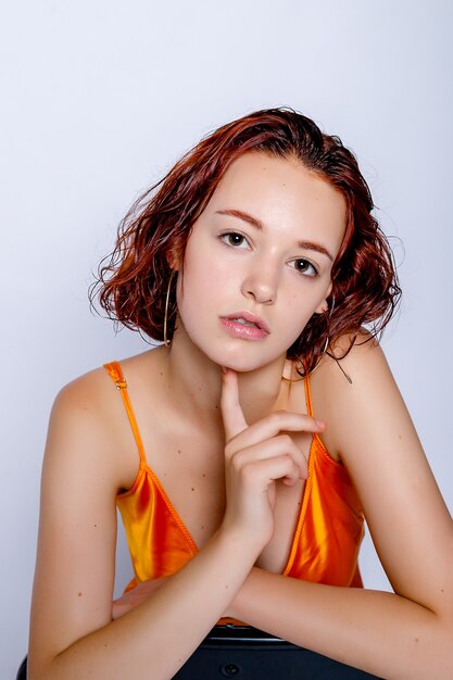 Portrait of attractive girl in orange dress in the studio. Fascinating red-haired lady. closeup portrait sitting on a chair