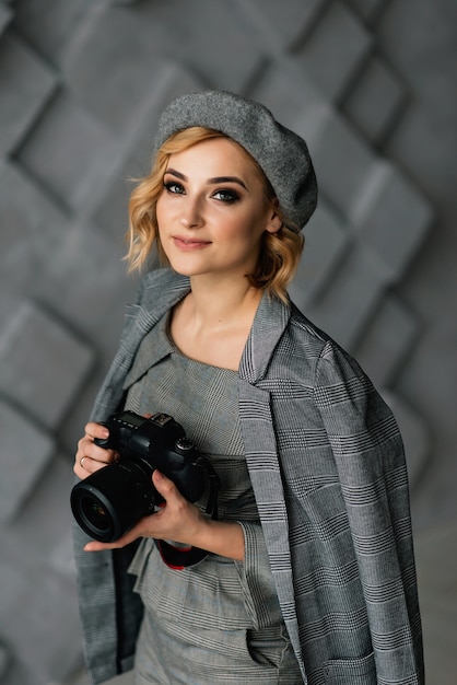 Portrait of an attractive girl photographer in stylish clothes and a beret with a camera in her hands. The concept of creative professions.