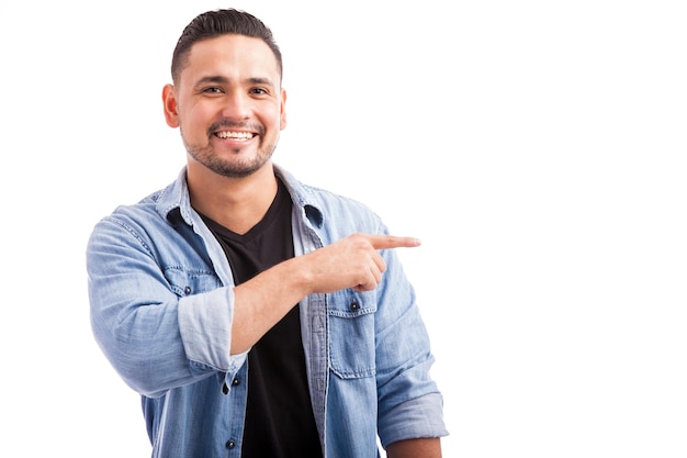 Portrait of an attractive guy in casual clothes pointing to the side towards copy space and smiling