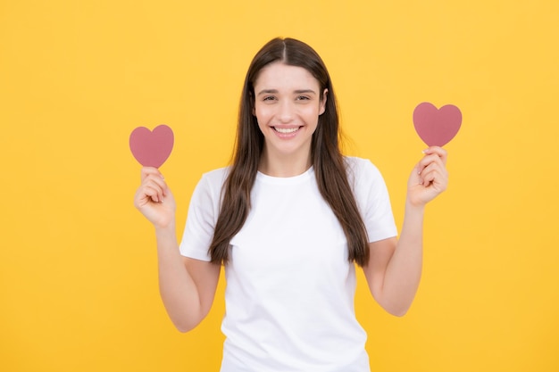 Portrait of attractive lovely cheerful girl holding in hands paper heart isolated over yellow