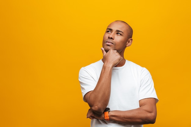 Portrait of an attractive pensive casual young african man standing over yellow wall