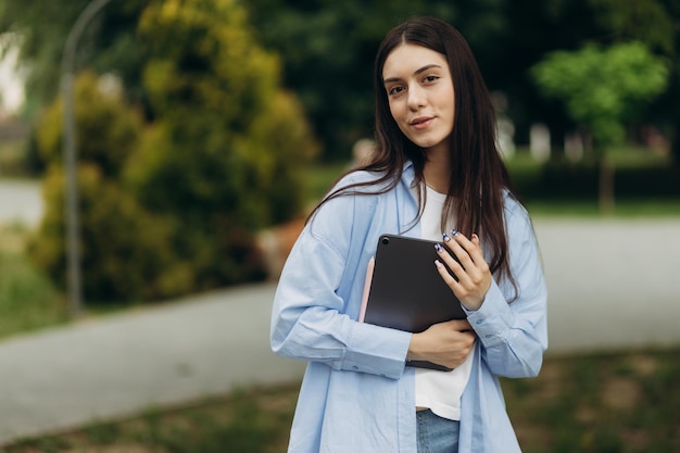 Portrait of an attractive student girl holding a gadget in her hands The girl looks at the camera Copy space